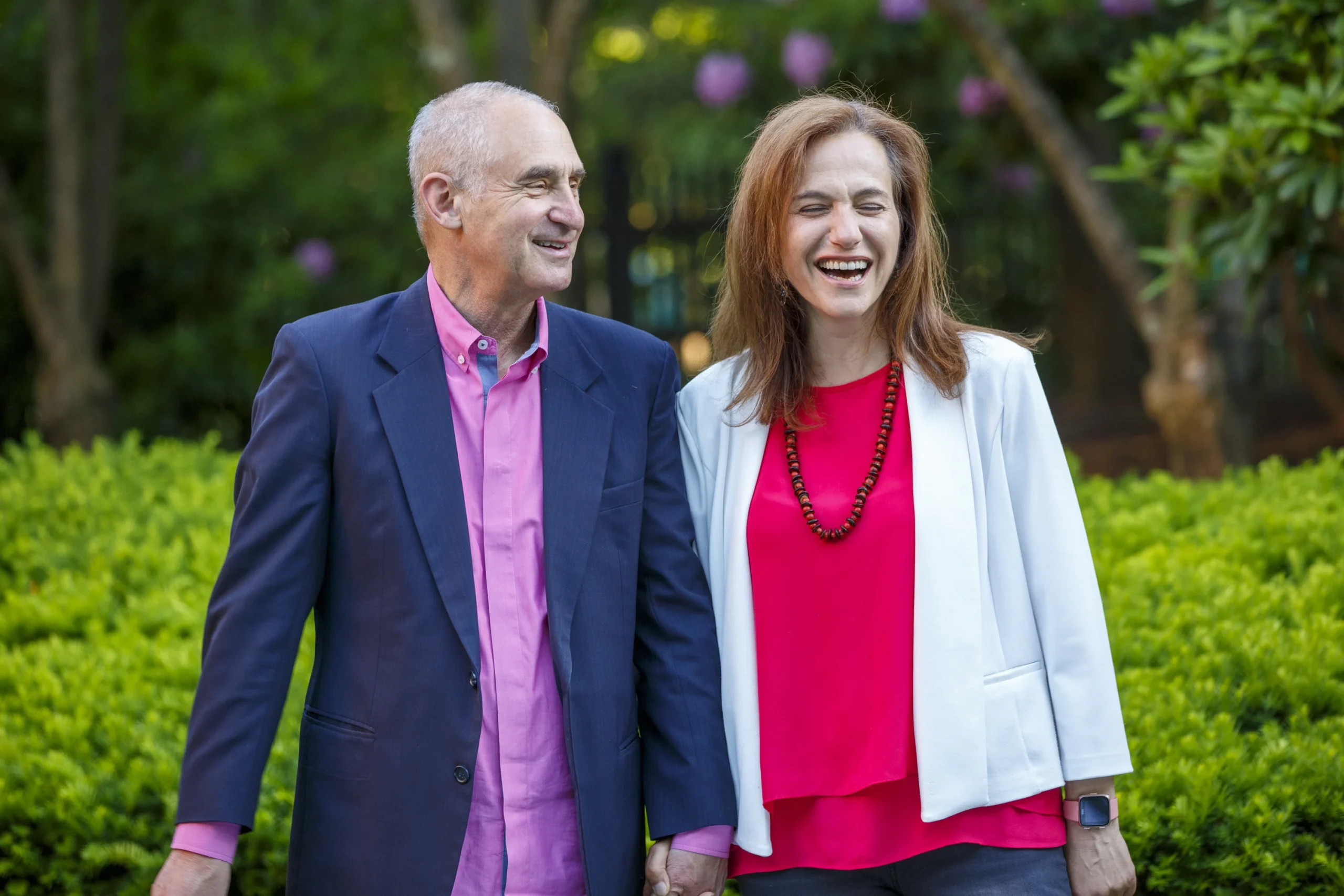 Daniel and Carla holding hands and laughing together outdoors in a peaceful garden setting.